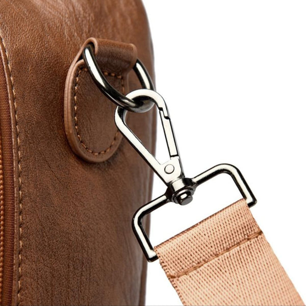 Close-up of a brown leather bag with a metal clasp and beige strap on a white background