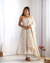 Woman wearing a white floral dress with a matching dupatta in a minimalistic setting.