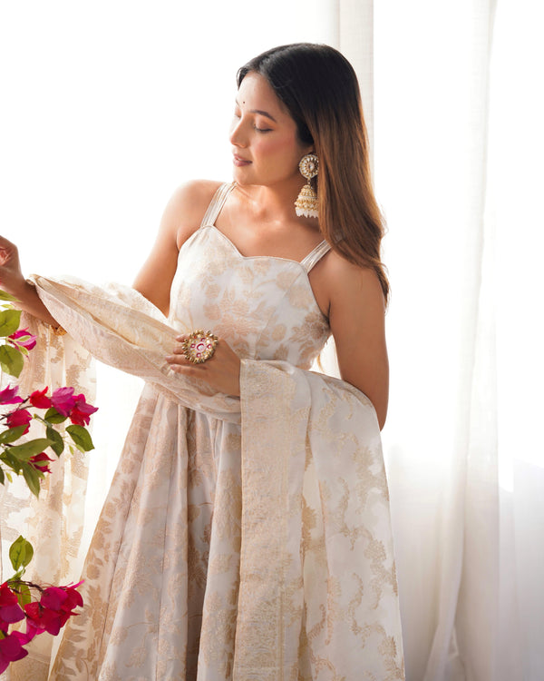 Woman in a white and gold saree holding flowers against a white background