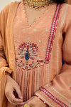Close-up of a peach-colored traditional outfit with intricate embroidery and jewelry.