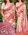 White saree with pink border and intricate patterns, worn by a model against a green leafy background.
