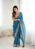 Woman wearing a blue saree with floral embroidery in a minimal indoor setting.