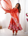 Woman in a red floral dress holding a sheer orange fabric against a white curtain background