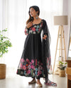 Woman wearing a black floral dress with a sheer dupatta in a bright room.
