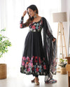 Woman wearing a black floral dress with a sheer dupatta in a bright room.