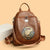 Brown leather backpack with decorative emblem on a beige background