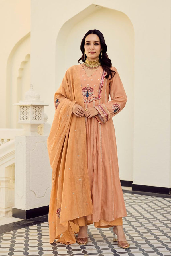 Woman in a gysy suits peach traditional outfit standing in an elegant interior setting.