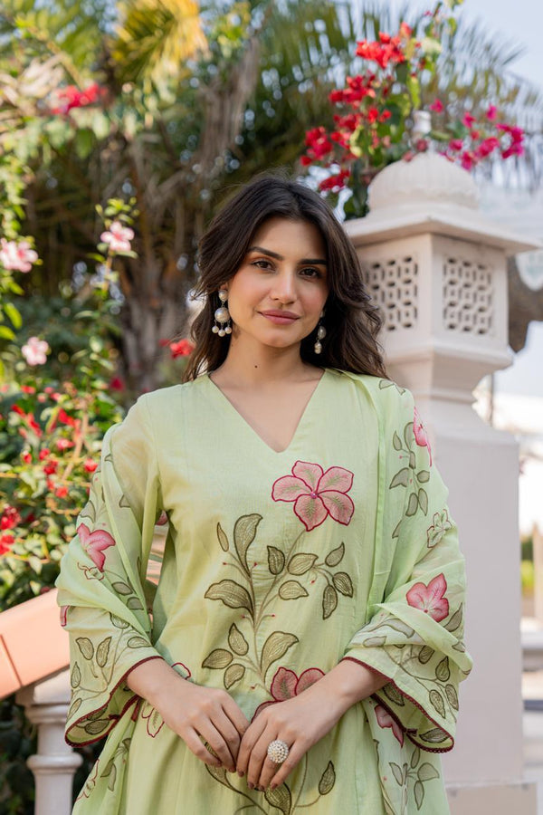 Woman wearing a light green embroidered dress with floral patterns in an outdoor setting.