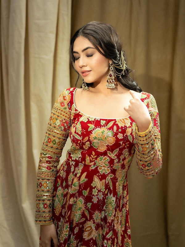 Woman wearing a red embroidered traditional outfit with gold details against a beige curtain background