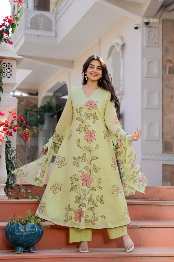 Woman in a light green embroidered outfit standing on steps with floral decorations.