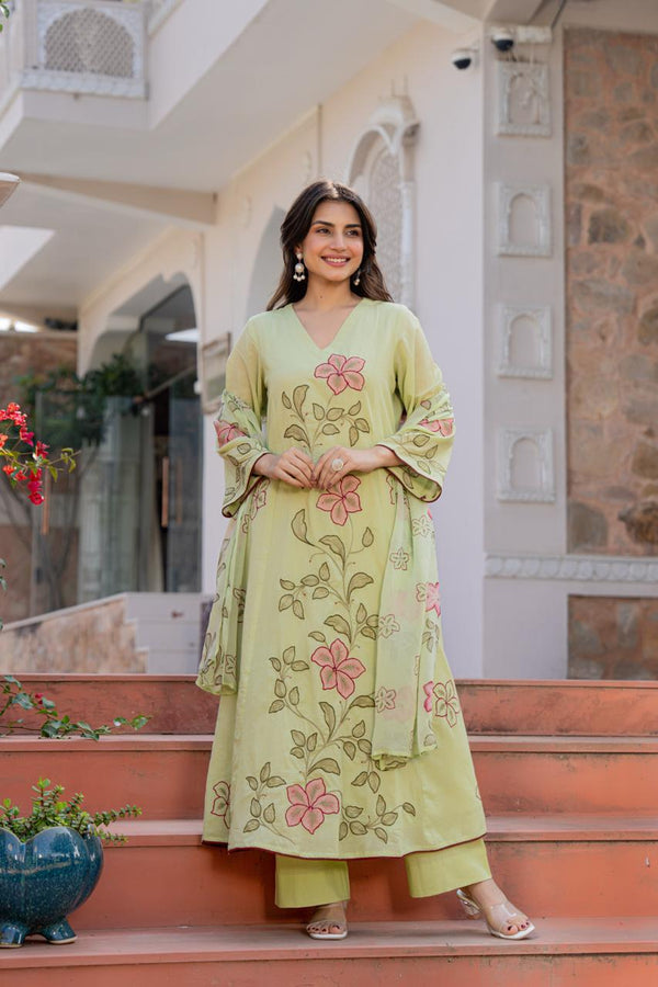 Woman in a light green embroidered outfit standing on steps with a decorative background