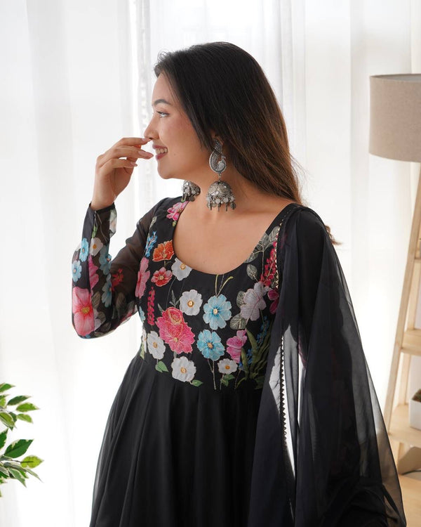 Woman wearing a black floral dress with a sheer black shawl in a bright room.