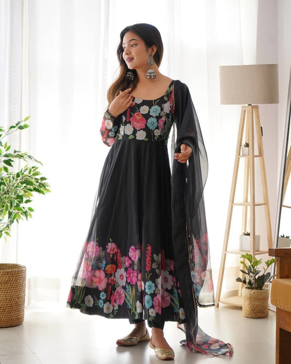 Woman wearing a black floral dress with a sheer dupatta in a bright room.