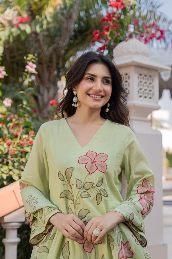 Woman wearing a light green embroidered dress with flowers in an outdoor setting.